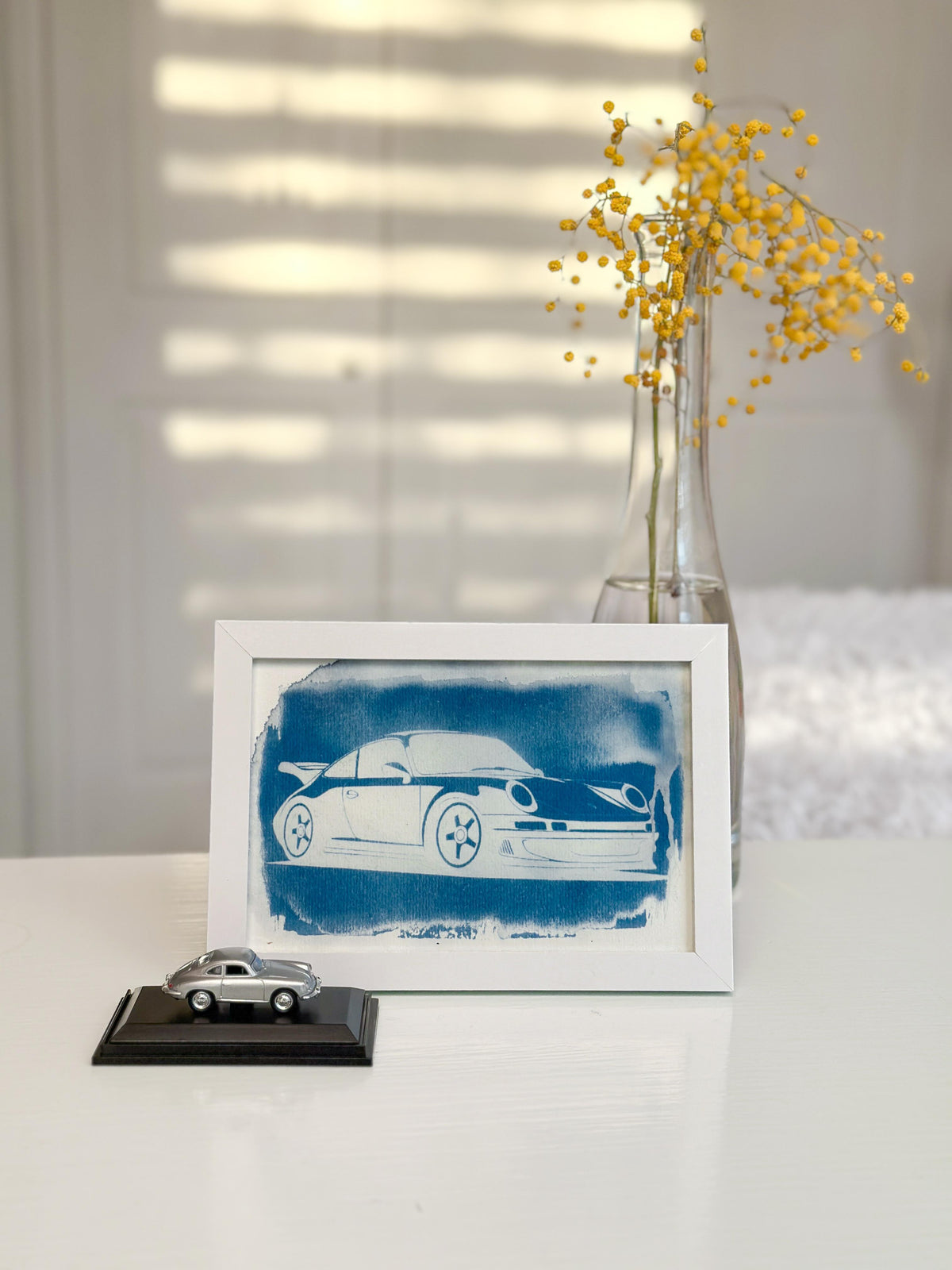 Cianotipia enmarcada de un Porsche con un coche en miniatura y flores